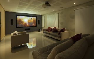 Essential Principles of Video Projection & Display Technology 1 A well-designed home theater room with a large, illuminated projection screen displaying vibrant visuals, two white sofas, and a dark-colored couch, relevant to the ‘Essential Principles of Video Projection & Display Technology’ article. Una sala de cine en casa bien diseñada con una gran pantalla de proyección iluminada que muestra visuales vibrantes, dos sofás blancos y un sofá de color oscuro, relevante para el artículo ‘Principios esenciales de la tecnología de proyección y visualización de video’.