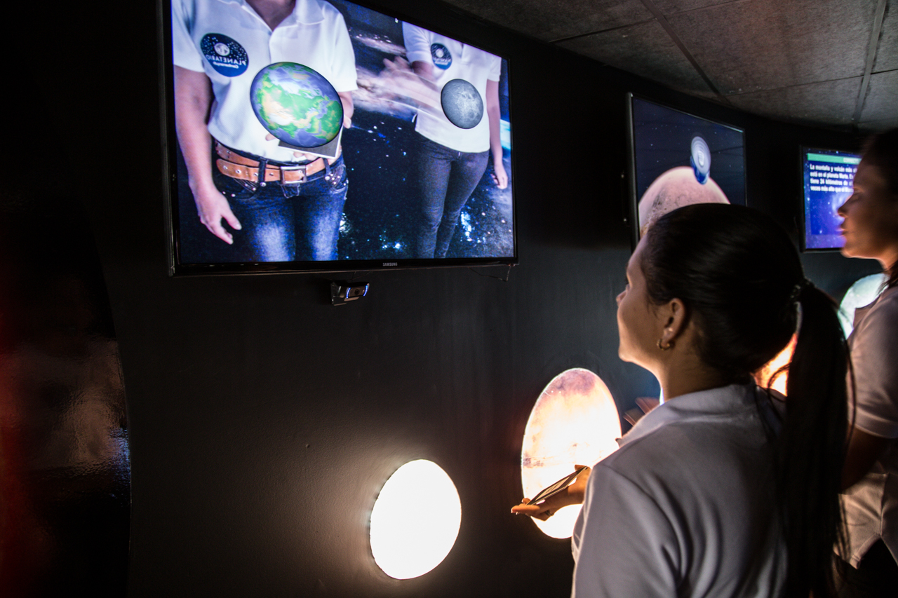 The Healing Harmony: Social and Cultural Impacts of Performing Arts Centers 3 A space-themed exhibit featuring multiple screens displaying images of people with celestial bodies superimposed on their torsos, symbolizing the cosmic connection explored in ‘The Healing Harmony: Social and Cultural Impacts of Performing Arts Centers’. Una exposición temática espacial que presenta múltiples pantallas que muestran imágenes de personas con cuerpos celestes superpuestos en sus torsos, simbolizando la conexión cósmica explorada en ‘The Healing Harmony: Social and Cultural Impacts of Performing Arts Centers’.