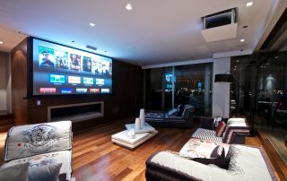 Luxurious living room at night featuring a large, wall-mounted screen displaying various media options and a ceiling-mounted projector, relevant to the ‘Cutting-Edge Innovations in Screens and Projection Systems’ article.