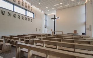 Modern church interior with wooden pews, a large cross, and acoustic panels, for an article on Enhancing Church Acoustics with Renkus-Heinz Solutions.
