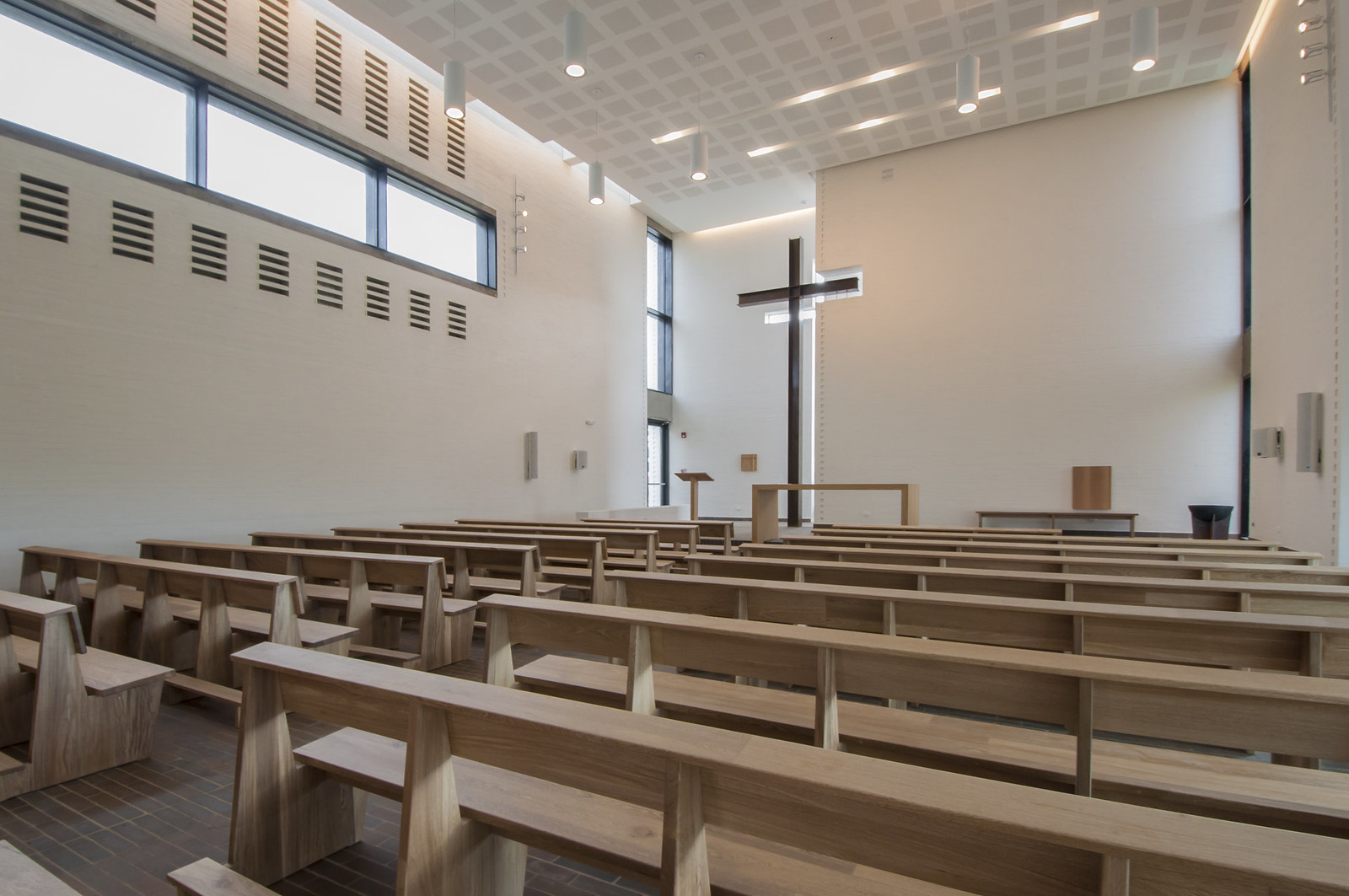 Modern church interior with wooden pews, a large cross, and acoustic panels, for an article on Enhancing Church Acoustics with Renkus-Heinz Solutions.