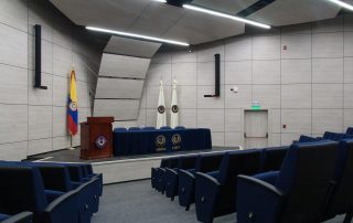 Modern boardroom with acoustic panels, blue seating, and a podium, optimized for sound quality and privacy in an article about optimizing boardroom acoustics. Sala de juntas moderna con paneles acústicos, asientos azules y un podio, optimizada para la calidad del sonido y la privacidad en un artículo sobre la optimización de la acústica en salas de juntas.