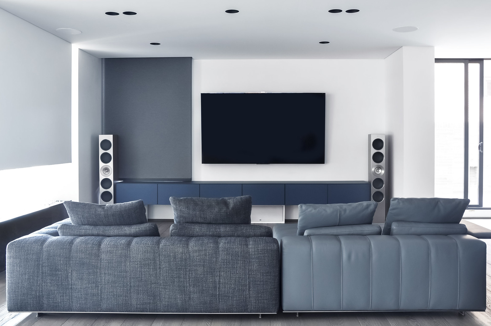 A modern living room with a home theater setup including a flat-screen TV and tall speakers, perfect for an article on amplifier setup and fixing home theater issues. Una sala de estar moderna con un sistema de cine en casa que incluye un televisor de pantalla plana y altavoces altos, perfecta para un artículo sobre la configuración de amplificadores y la solución de problemas de home theater.