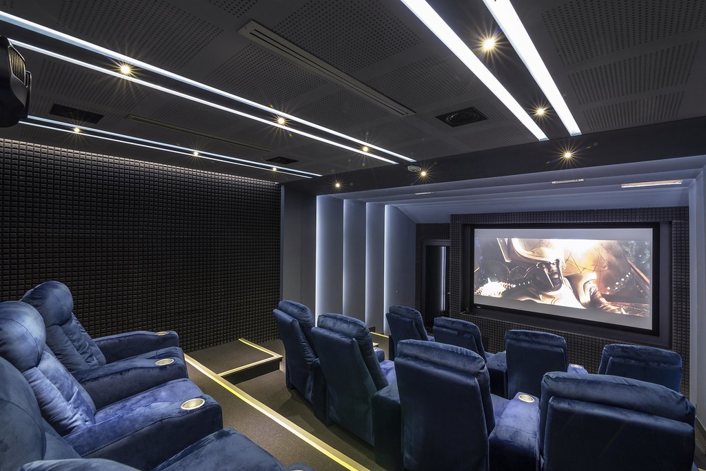 Modern, luxurious home theater with acoustic conditioning, plush seating, and advanced lighting, illustrating future trends in acoustic conditioning. Teatro en casa moderno y lujoso con acondicionamiento acústico, asientos de lujo e iluminación avanzada, ilustrando las tendencias futuras en acondicionamiento acústico.