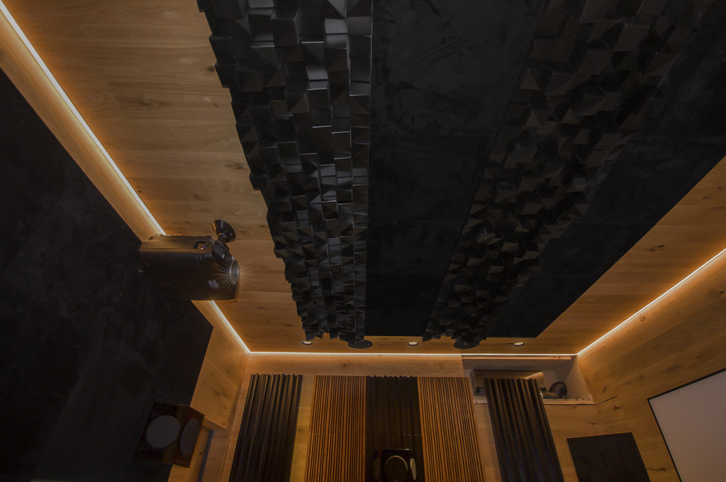Dominando la Acústica del Estudio de Grabación para una Calidad de Sonido Pura 1 Vista interior de un estudio moderno o teatro con diseño acústico especializado, que presenta paneles acústicos geométricos negros y una pared de madera, para un artículo sobre el dominio de la acústica en estudios de grabación.