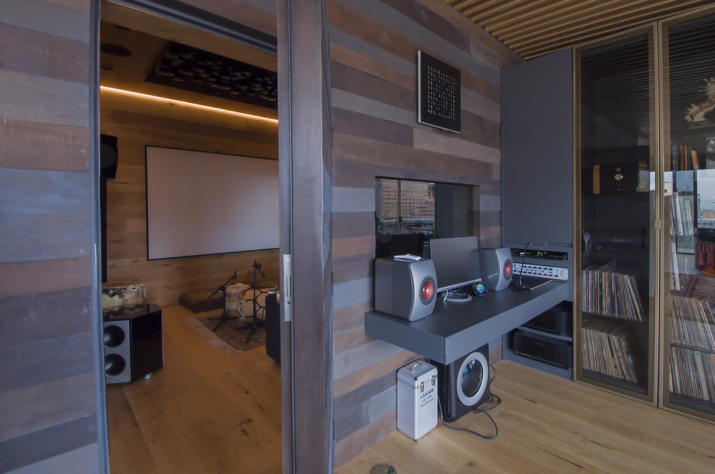 Dominando la Acústica del Estudio de Grabación para una Calidad de Sonido Pura 3 Vista interior de una sala audiovisual moderna con equipo de audio sofisticado, una gran pantalla de proyección y discos de vinilo, para un artículo sobre el dominio de la acústica en estudios de grabación.