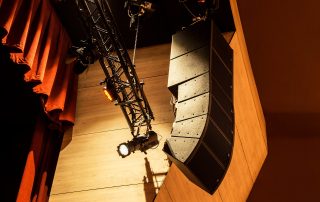 Maximizing Audio Quality: The Truth Behind Speaker Cable Choices 4 Professional audio speakers hanging from a ceiling rig in a theater, illustrating the concept of maximizing audio quality through speaker cable choices for the article ‘Maximizing Audio Quality: The Truth Behind Speaker Cable Choices’. Altavoces de audio profesionales colgando de una estructura en el techo en un teatro, ilustrando el concepto de maximizar la calidad del audio a través de las opciones de cables para altavoces para el artículo ‘Maximizando la Calidad del Audio: La Verdad Detrás de las Opciones de Cables para Altavoces’.