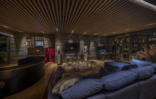 Acoustically optimized interior of a performing arts center with wooden slatted ceilings, plush seating, and ambient lighting. Interior acústicamente optimizado de un centro de artes escénicas con techos de listones de madera, asientos lujosos e iluminación ambiental.