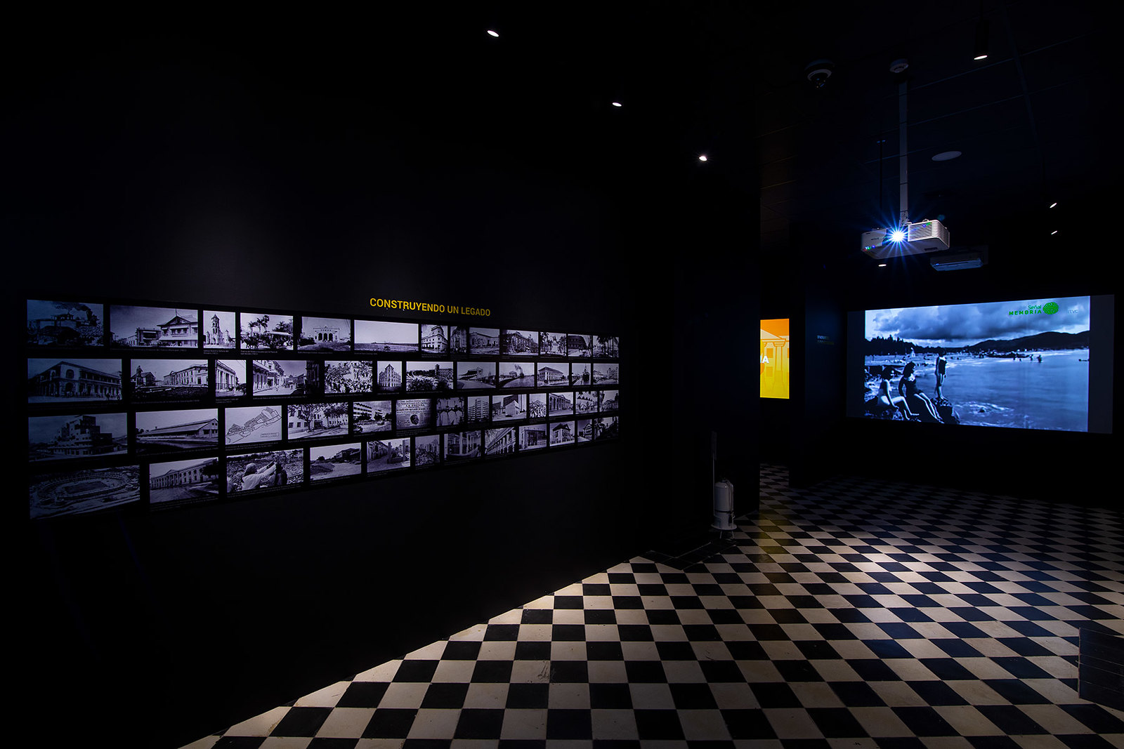 A modern AV integration design showcasing a wall of black and white historical photos, illuminated by focused lighting, in a room with checkered flooring, enhancing the visual experience for ‘Essential AV Integration Design Fundamentals’. Un diseño moderno de integración AV que muestra una pared de fotos históricas en blanco y negro, iluminada por una iluminación enfocada, en una sala con suelo ajedrezado, mejorando la experiencia visual para ‘Fundamentos esenciales del diseño de integración AV’.