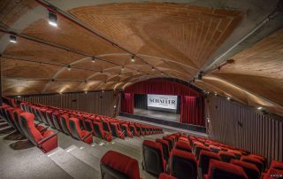 Interior view of the SCHAILER Performing Arts Center auditorium with optimized space and logistics, featuring plush red seating and a wooden acoustic ceiling.