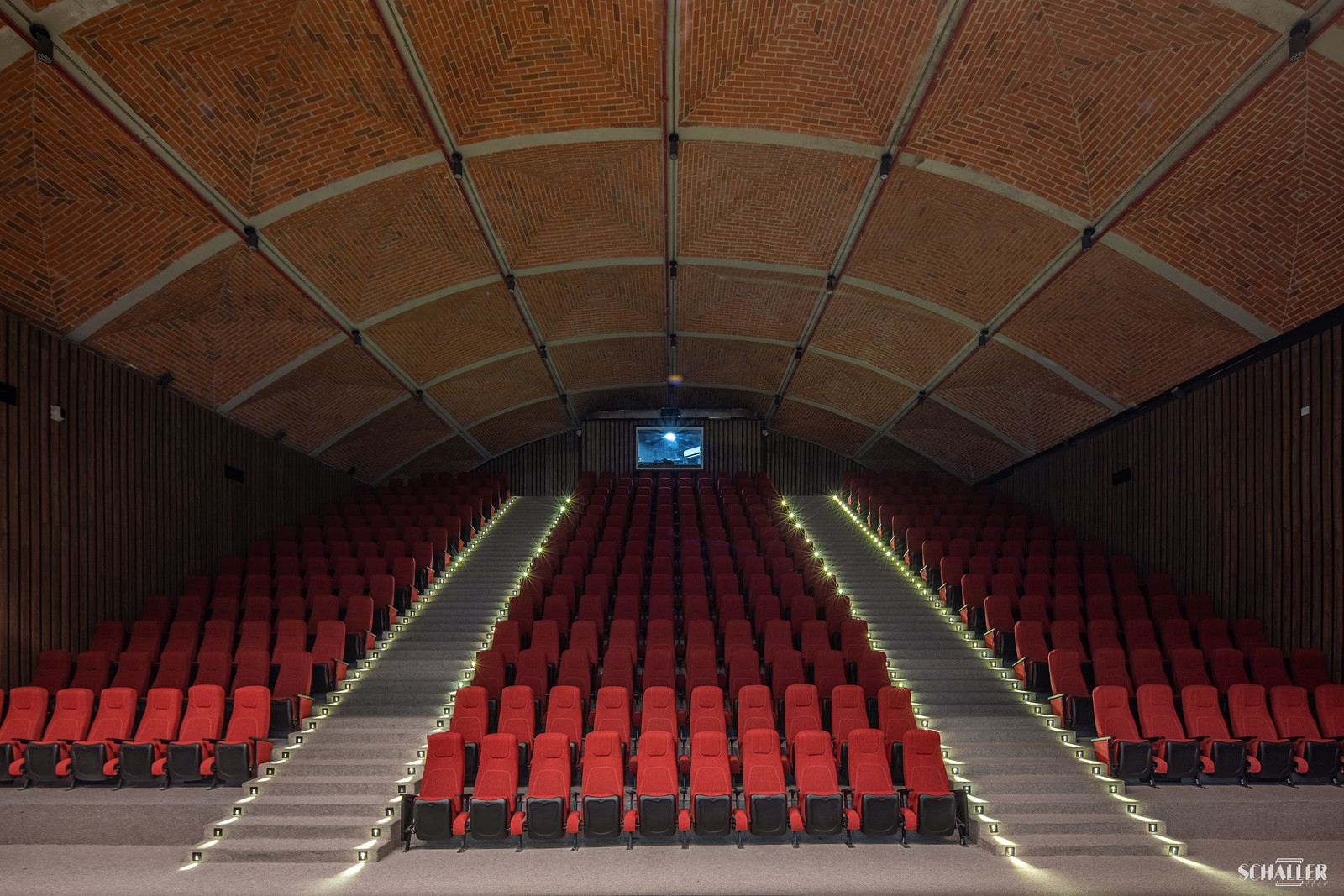 Interior view of a theater with a spotlight on the empty stage and rows of orange seats, reflecting the inclusive future of design trends in performing arts centers. Vista interior de un teatro con un foco de luz en el escenario vacío y filas de asientos naranjas, reflejando el futuro inclusivo de las tendencias de diseño en los centros de artes escénicas.