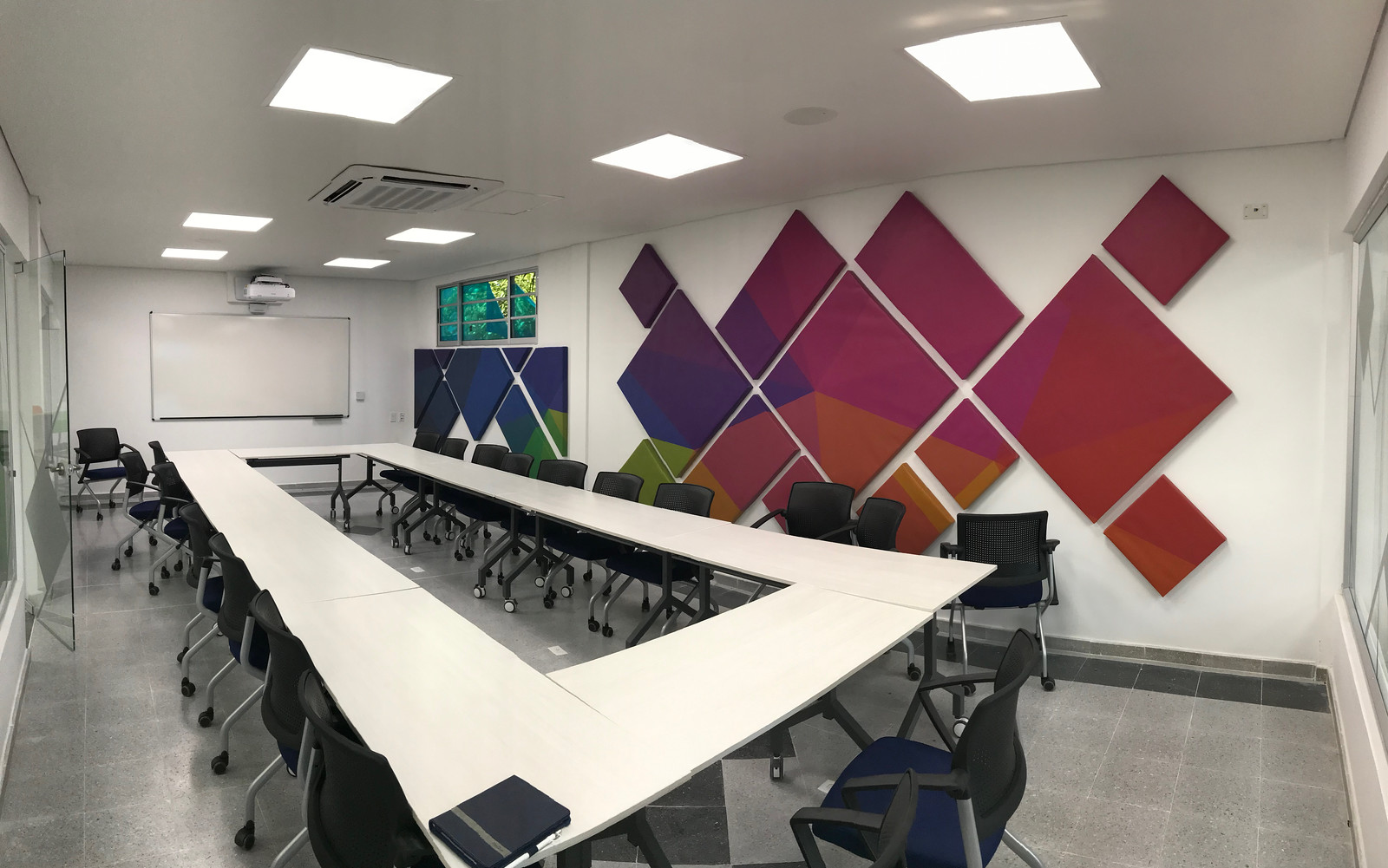 Eco-Friendly Soundproofing: Recycled PET Acoustic Panels 1 Colorful and modern conference room featuring eco-friendly recycled PET acoustic panels, a large whiteboard, a U-shaped table, and bright lighting, suitable for an article on Eco-Friendly Soundproofing. Sala de conferencias moderna y colorida que presenta paneles acústicos de PET reciclado ecológico, un gran tablero blanco, una mesa en forma de U y una iluminación brillante, adecuada para un artículo sobre insonorización ecológica.