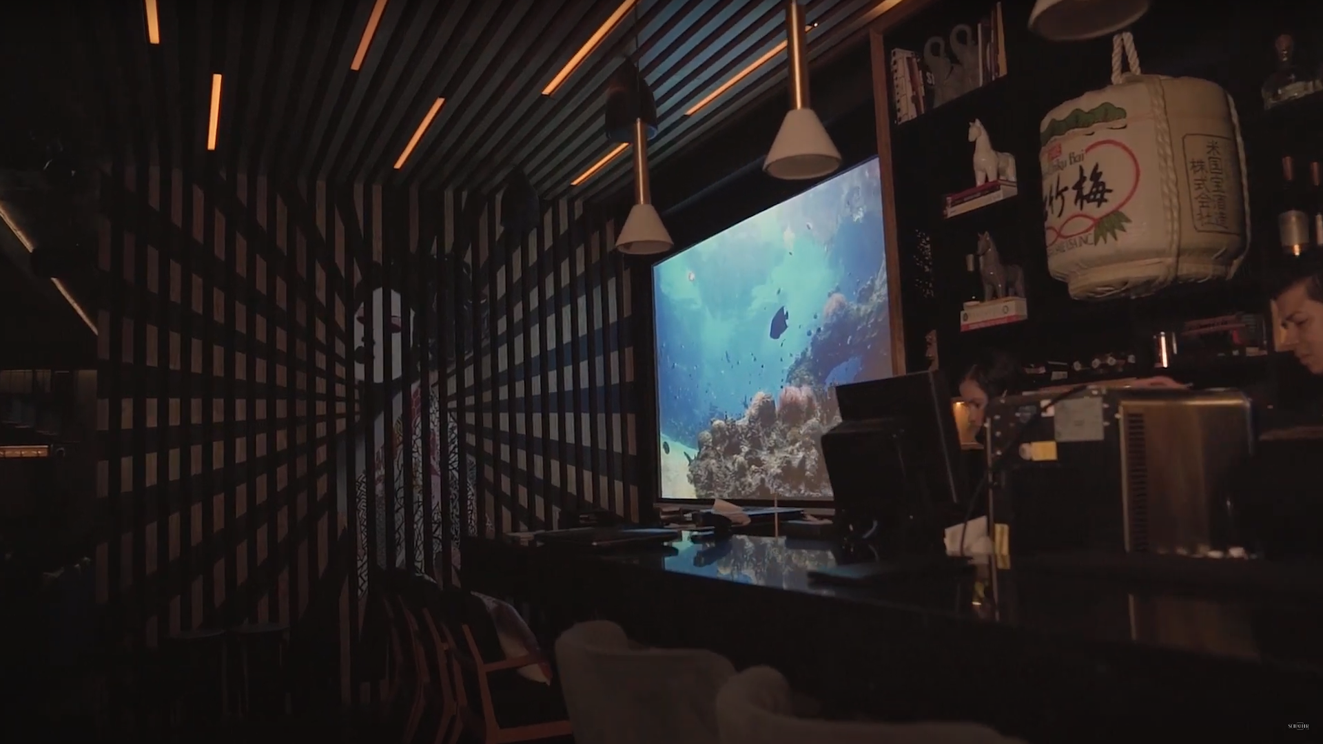 Modern and stylish bar with a large screen displaying an underwater scene, optimized for an article on ‘Optimizing Restaurant Acoustics: Strategies for Soundproofing and Ambiance’. Bar moderno y elegante con una gran pantalla que muestra una escena submarina, optimizado para un artículo sobre ‘Estrategias para la insonorización y el ambiente en la optimización de la acústica de los restaurantes’.