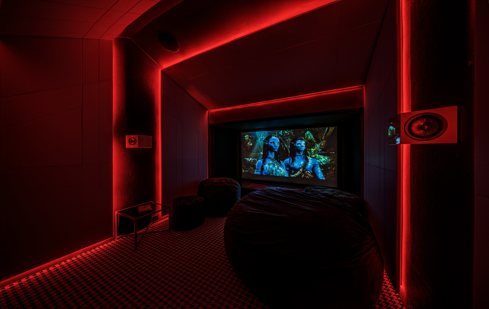 Intimate home theater setting with a large screen displaying a vibrant scene, plush black bean bags, and wall-mounted speakers, relevant to the ‘Exploring AV Integration Design: Definition, Scope, and Sector Impact’ article. Ambiente íntimo de cine en casa con una gran pantalla que muestra una escena vibrante, pufs negros y altavoces montados en la pared, relevante para el artículo ‘Explorando el Diseño de Integración AV: Definición, Alcance e Impacto Sectorial’.