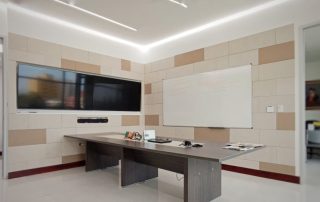 Modern office room with acoustic wall panels for sound dampening, featuring a sleek desk, a large TV screen, and a whiteboard.