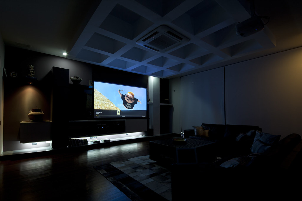 Modern living room with a large flat-screen TV displaying a skydiving scene, ambient lighting, and comfortable seating, reflecting future trends in home entertainment. Sala de estar moderna con un televisor de pantalla plana grande que muestra una escena de paracaidismo, iluminación ambiental y asientos cómodos, reflejando las tendencias futuras en entretenimiento doméstico.
