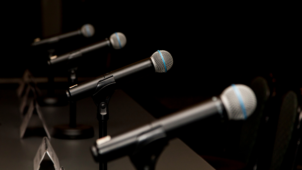 Top 5 Microphones for Boardrooms: From Small to Large Spaces 1 Four professional-grade microphones on stands, illuminated dramatically against a dark background, representing the top choices for boardroom audio technology. Cuatro micrófonos de grado profesional en soportes, iluminados dramáticamente contra un fondo oscuro, representando las mejores opciones para la tecnología de audio en salas de juntas.
