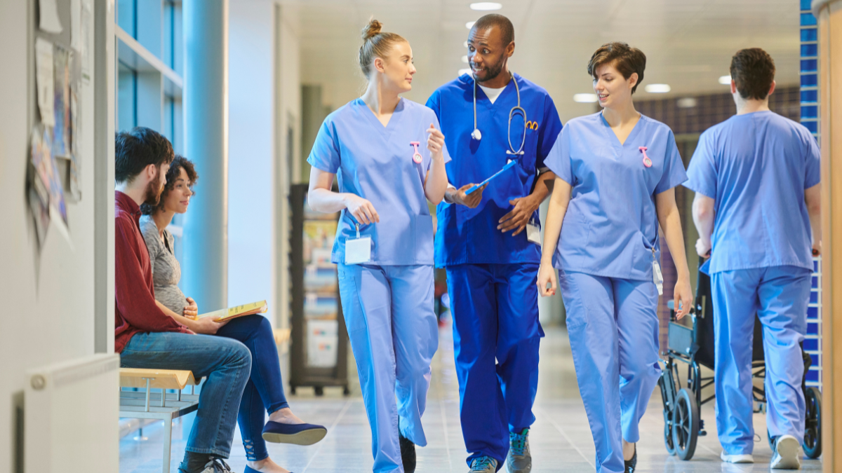 Optimización de la Acústica en Espacios de Atención Médica para el Confort del Paciente 3 Profesionales de la salud en batas azules caminando por un pasillo bien iluminado en una instalación médica, para un artículo sobre la optimización de la acústica del espacio de atención médica para la comodidad del paciente.