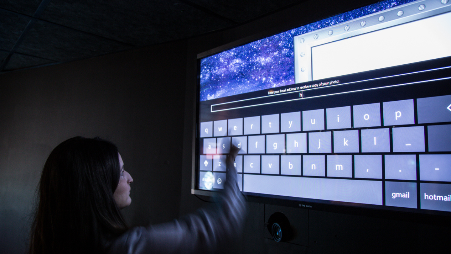 User interacting with a large touchscreen display in a dimly lit room, demonstrating advanced AV design for the article ‘Overcoming AV Design Hurdles: Keys to Project Success’. Usuario interactuando con una gran pantalla táctil en una habitación con poca luz, demostrando diseño AV avanzado para el artículo ‘Superando los obstáculos del diseño AV: Claves para el éxito del proyecto’.